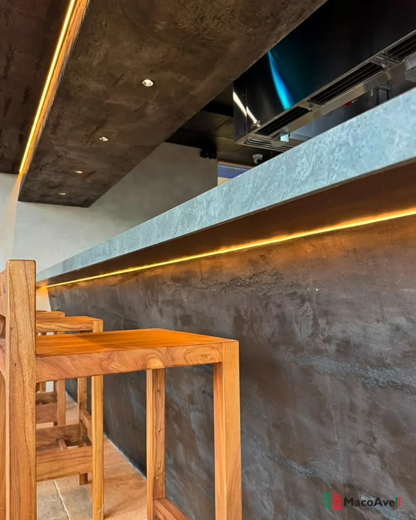 StoneArt counter-front detail at KLCGG with horizontal texture, warm linear lighting and timber stools.