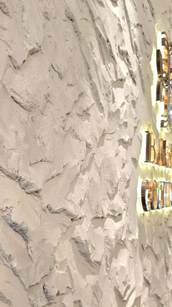 Angled close-up of raised StoneArt texture beside the illuminated signage in Kuala Lumpur.