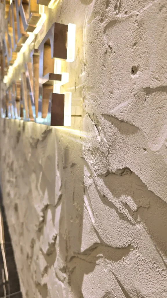 Close-up of the granular StoneArt finish and raised relief beside backlit metal lettering in Kuala Lumpur.
