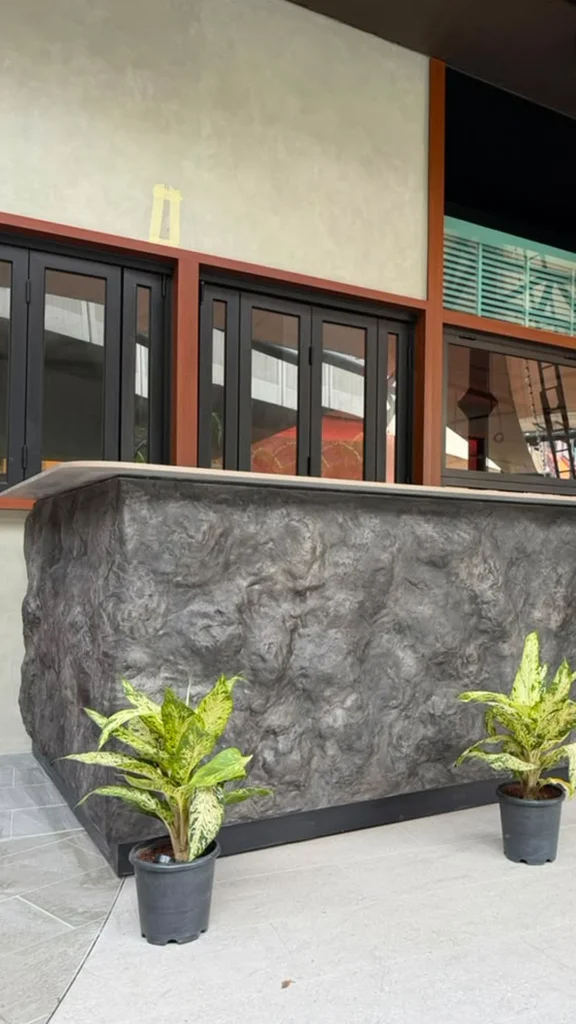 StoneArt counter with sculpted grey texture beneath dark windows and warm brown trim in Kuala Lumpur.