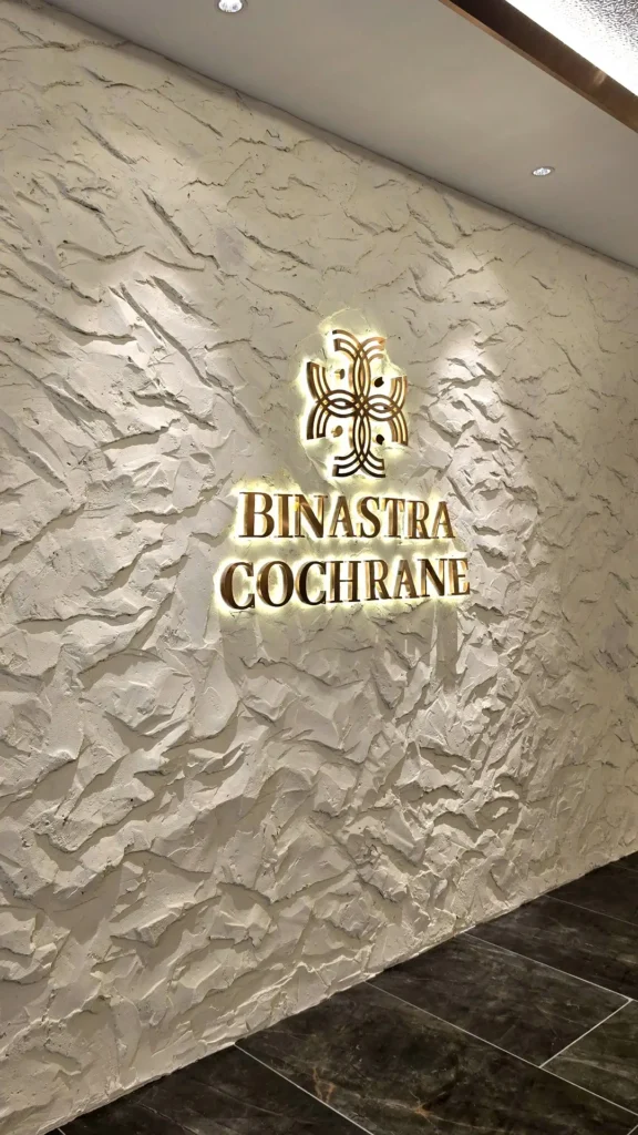 Full view of the pale StoneArt feature wall and illuminated Binastra Cochrane signage above dark floor tiles in Kuala Lumpur.