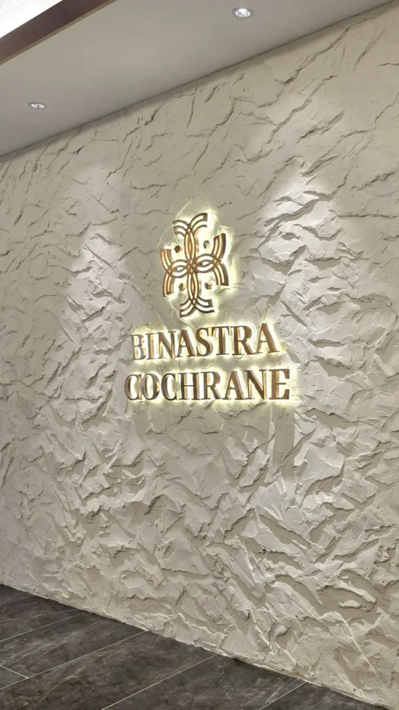 Illuminated Binastra Cochrane sign on a pale StoneArt wall under ceiling downlights in Kuala Lumpur.