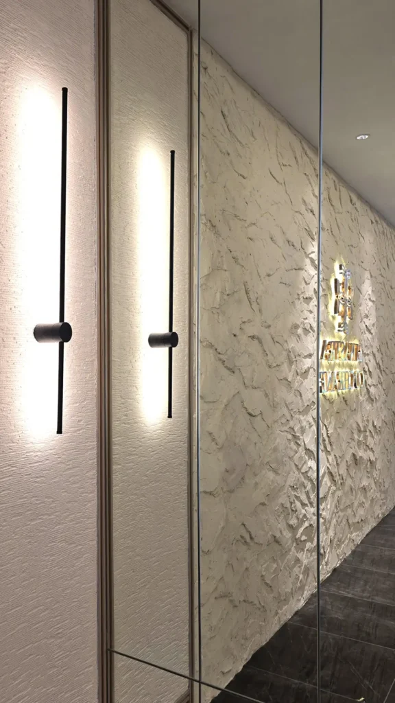 Mirror reflection of the StoneArt feature wall and illuminated signage beside slim black wall lights in Kuala Lumpur.