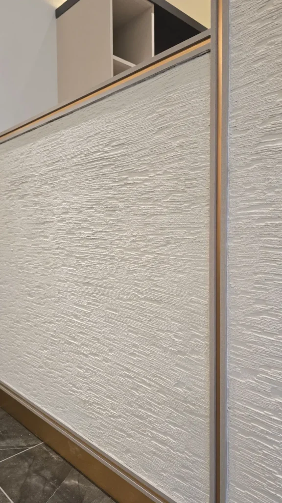 Pale Vellcco Custom textured wall panel bordered by slim metallic trim above dark tiled flooring.