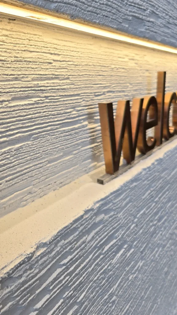 Close-up of welcome lettering against the pale Vellcco Custom finish beneath a warm light strip.